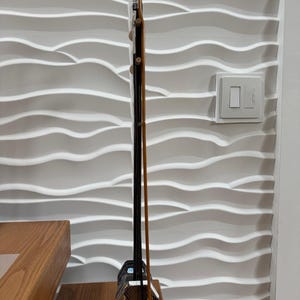 May include: A vertical erhu, a traditional two-stringed bowed musical instrument, featuring a long dark wooden neck, a small hexagonal sound box covered with a textured snakeskin pattern, and a long, thin wooden bow resting against the side.
