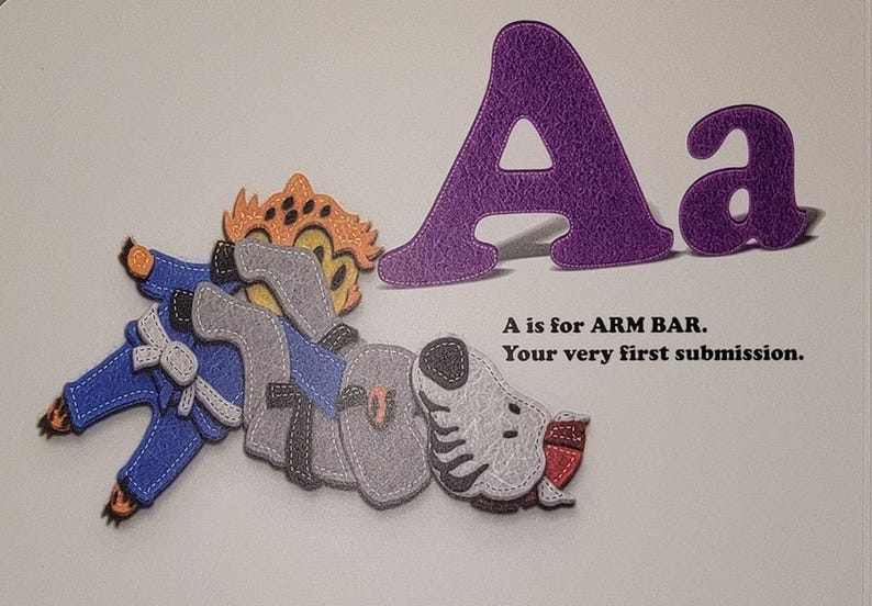 May include: A purple felt letter A with a smaller lowercase a next to it. An illustration of a person in a blue martial arts uniform performing an arm bar submission hold on a gray and white animal. The text reads "A is for ARM BAR. Your very first submission."
