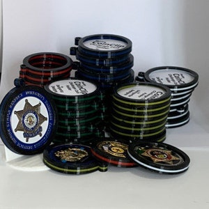 May include: A collection of black, green, blue, and white coin clips with the word "CoinClip" printed on them. Some of the clips have a star-shaped design with the words "Ethics, Honor, Respect, Integrity, Service, Fairness" printed around the star.