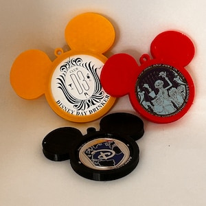 May include: Three Mickey Mouse-shaped pinbacks. The first is yellow with a black and white design that says "Club 33 Disney Day Drinker". The second is red with a black and white design that says "You Are Just In Time For The Haunted Mansion". The third is black with a silver Disney logo.