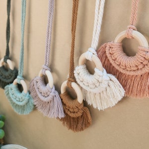 May include: A set of nine macrame wall hangings with wooden rings and fringe. The hangings are in various colors, including beige, brown, pink, and blue.
