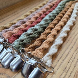May include: A set of seven crocheted dummy clips in various colours, including cream, brown, green, pink, and red. Each clip features a silver metal clasp.