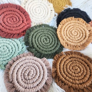 May include: A set of nine colourful round crocheted coasters with fringe. The coasters are made of cotton rope and have a spiral design. The colours include red, white, black, green, brown, and beige.