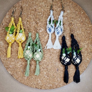 Könnte beinhalten: Vier Paare Makrame-Ohrringe mit kleinen Topfpflanzen. Die Ohrringe sind in Gelb, Weiß, Grün und Schwarz.