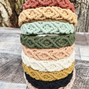 Puede incluir: Una pila de ocho diademas de crochet en varios colores, incluyendo óxido, beige, verde claro, verde oscuro, melocotón, blanco, amarillo mostaza, negro y marrón claro.
