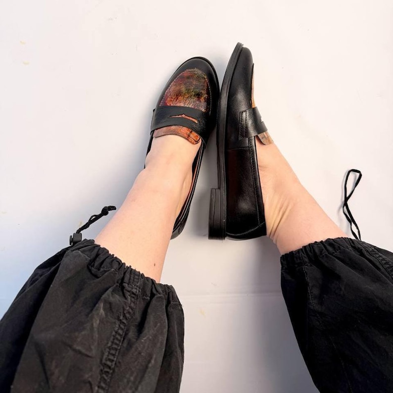 Puede incluir: Mocasines de cuero negro con un dise&ntilde;o &uacute;nico en la pala. Los zapatos tienen un estilo cl&aacute;sico de mocas&iacute;n con tac&oacute;n bajo. El patr&oacute;n presenta una mezcla de colores, incluyendo marr&oacute;n, naranja y verde.