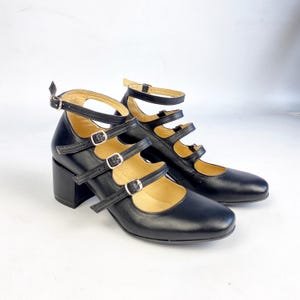 Könnte beinhalten: Ein Paar schwarze Mary Jane-Schuhe aus Leder mit mehreren Riemen und Schnallenverschlüssen. Die Schuhe haben einen Blockabsatz und eine runde Spitze. Die Riemen sind verstellbar. Neue Schuhe.