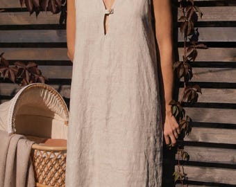 Puede incluir: Un vestido sin mangas de lino beige con un escote en V profundo y un pequeño botón de cierre en el centro. La prenda tiene una silueta recta y relajada que llega hasta la rodilla, mostrando un acabado de tela con textura natural.