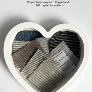 May include: AIGA Striped linen samples in a heart-shaped container. The samples are in various shades of blue, brown, and grey with white stripes. The text on the image reads "AIGA Striped linen samples 190 g/m² and 205 g/m², 9 variations".