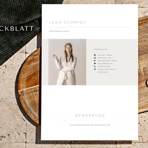 May include: A resume template with the name "LENA SCHMIDT" at the top. The document includes personal details and the word "BEWERBUNG" at the bottom. The word "DECKBLATT" is in the upper left corner. The resume is on a wooden surface.