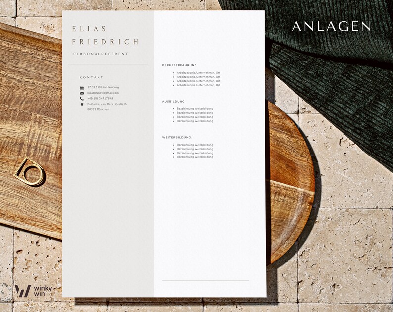 May include: A white resume with the name Elias Friedrich and the title Personalreferent. The resume includes contact information, work experience, education, and skills. The resume is on a wooden table with a green cloth in the background.