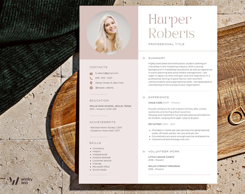 May include: A resume template with a photo of a smiling person, featuring a soft color palette. The resume includes sections for contact information, education, achievements, skills, and experience. The resume is on a wooden surface.