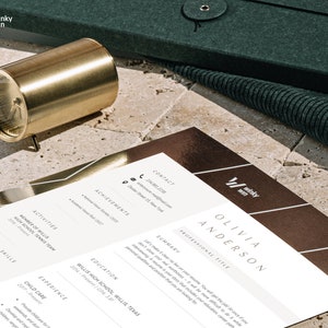 May include: A gold-colored cylindrical object with a clock face is next to a resume. The resume is white with brown accents and the name "Olivia Anderson" at the top. The resume also has the "winky win" logo. A dark green case is in the background.