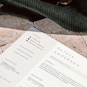 May include: A resume with the name Olivia Anderson, contact information, achievements, activities, technical skills, and education. The resume is on a light beige surface with a dark green corduroy fabric in the background.