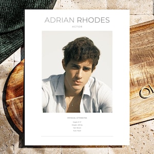 May include: A headshot of Adrian Rhodes, an actor, is displayed on a white sheet of paper. The actor is wearing a light blue striped shirt. The text "ADRIAN RHODES ACTOR" is printed at the top. Below the photo are physical attributes: Height 6' 0", Weight 165 lbs, Hair Brown, Eyes Hazel.