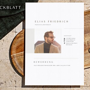 May include: A white resume template with the title "DECKBLATT" at the top. The resume is for Elias Friedrich, Personalreferent. The resume includes a professional headshot of Elias, contact information, and the text "BEWERBUNG ALS PROJEKTMANAGER BEI DER SALZGITTER".