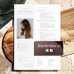 May include: A resume with the name "Lisa Friedrich" and the title "Personalreferent" is displayed on a wooden surface. The resume includes a photo, personal details, and sections for languages and qualifications. A small, gold-colored ring is also visible.