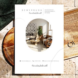 Puede incluir: Un folleto blanco con el texto "BEWERBUNG" y "FamilieSchmidt" en letra cursiva. Una imagen circular muestra una sala de estar con un sofá marrón, una mesa de centro y fotos enmarcadas. Una bandeja de madera y tela verde están en el fondo.