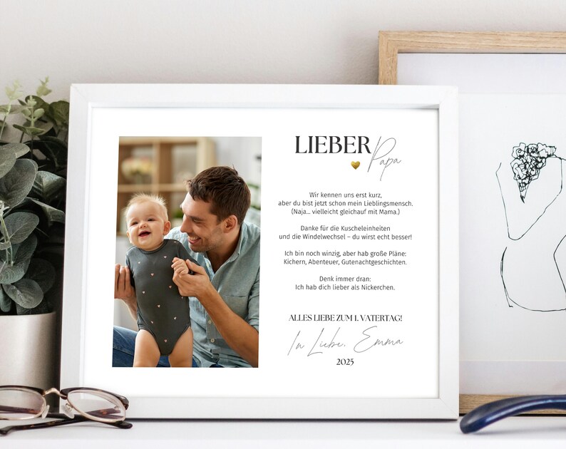 Może przedstawiać: Biała oprawiona grafika ze zdjęciem ojca i dziecka, z niemieckim tekstem. Tekst zawiera "LIEBER Papa" i wiadomość od "Emmy" z 2025 roku. Rama jest biała, a grafika jest wyświetlana na białej powierzchni.