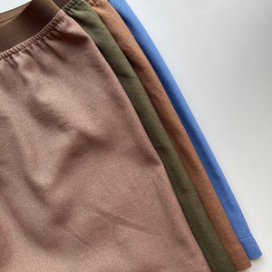 May include: A stack of four pairs of underwear in different colors: brown, olive green, brown, and light blue. The underwear is made of a soft, textured fabric.