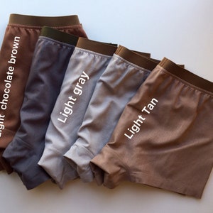 May include: Five pairs of boxer shorts in different colors: light chocolate brown, gray, light gray, light tan, and brown. The boxer shorts are folded and arranged in a row.