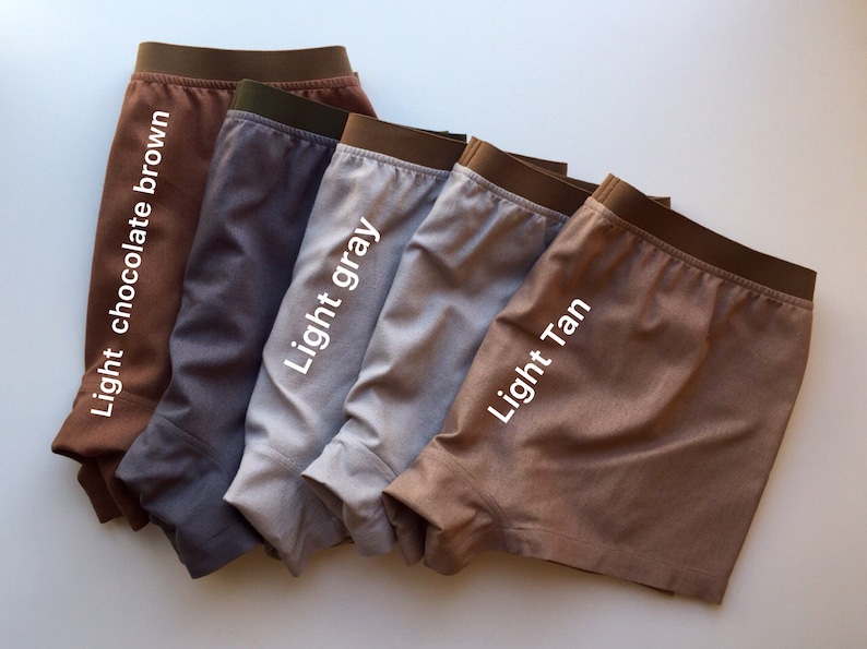 May include: Five pairs of boxer shorts in different colors: light chocolate brown, gray, light gray, light tan, and brown. The boxer shorts are folded and arranged in a row.