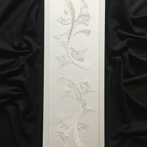 Könnte beinhalten: Weiße Papier-Schnittkunst in einem weißen Rahmen. Die Kunst zeigt eine Reihe von abstrakten Formen und Mustern.