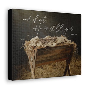 May include: A canvas print featuring a rustic wooden manger filled with hay and draped with cloth. The text "and if not, He is still good" is written in elegant script, with "Daniel 3:18" below. The artwork has a neutral color palette.