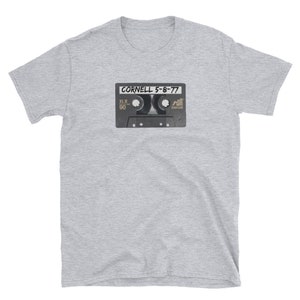 May include: A light gray t-shirt featuring a graphic of a vintage cassette tape. The tape has the text "CORNELL 5-8-77" printed on it. The shirt is made of a soft material and has short sleeves.