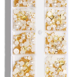Op de afbeelding: Een witte plastic container met 10 vakken gevuld met verschillende nagelkunstversieringen. De versieringen omvatten kleine gouden kralen, witte parels en gouden en witte vormen. De container is gelabeld "CapreDiemNail B-04".