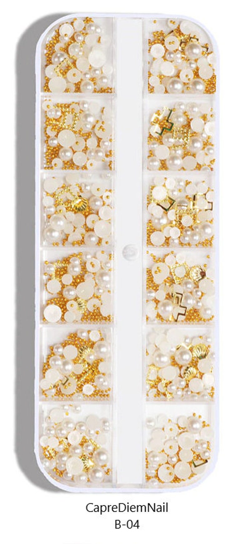 Op de afbeelding: Een witte plastic container met 10 vakken gevuld met verschillende nagelkunstversieringen. De versieringen omvatten kleine gouden kralen, witte parels en gouden en witte vormen. De container is gelabeld "CapreDiemNail B-04".