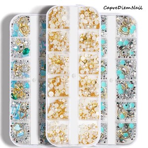 Op de afbeelding: Drie witte plastic containers gevuld met verschillende nagelkunstversieringen. De containers zijn elk in 12 secties verdeeld. De versieringen omvatten parels, strasssteentjes en kleine gouden en zilveren bedels.