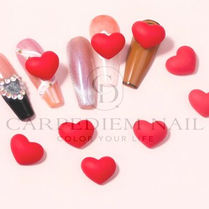 Może przedstawiać: Czerwone, sercowate ozdoby do paznokci rozrzucone na r&oacute;żowym tle. Na zdjęciu widoczny jest napis "Carpe Diem Nail Color Your Life".