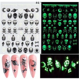 May include: Two sheets of glow-in-the-dark nail stickers with a variety of designs, including skulls, aliens, moons, and planets. The stickers are shown on a white background and on a set of pink nails.