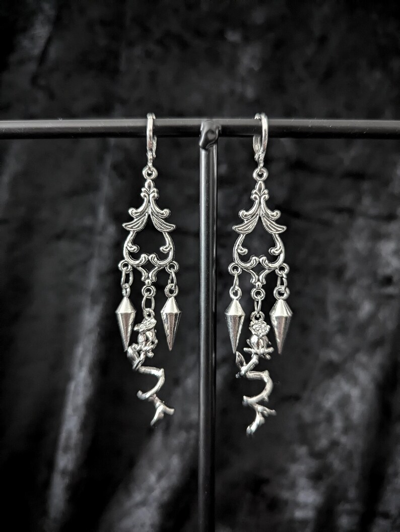 Op de afbeelding: Zilverkleurige oorhangers met sierlijke filigraan toppen, hangende geometrische vormen en takachtige accenten. Deze oorbellen hebben een gotische of Victoriaanse stijl, perfect om een vleugje elegantie en edge aan elke outfit toe te voegen.