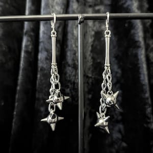 May include: A pair of silver-toned drop earrings featuring a long, slender post connected to a short chain. Each earring terminates in two dangling, multi-pointed spiked ball charms that resemble miniature medieval flail weapons or maces.