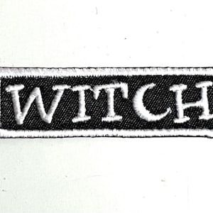 May include: A black and white embroidered patch with the word "WITCH" in white lettering.