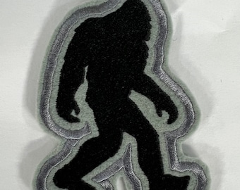 May include: A black felt patch with a gray outline of a Bigfoot silhouette. The patch is perfect for adding a touch of whimsy to backpacks, jackets, or other fabric items.
