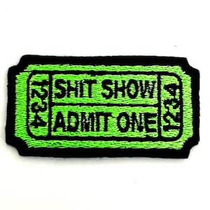 May include: Embroidered patch in the shape of a ticket with the words "SHIT SHOW" and "ADMIT ONE" in black text on a neon green background. The patch has a black border and the numbers "1234" on each side.