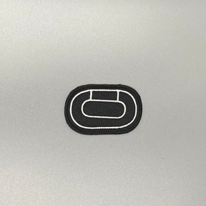 May include: Black embroidered patch with a white outline of an oval shape with a smaller oval inside.