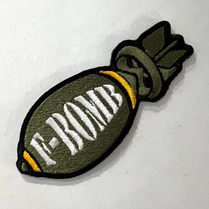 May include: Green embroidered patch shaped like a bomb with a yellow band and the text "E-BOMB" in white.