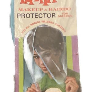 May include: Vintage "Tamya" makeup and hairdo protector for dressing. The packaging is a light blue, green, and yellow color. The text on the packaging reads "Fits all hairdos including bouffants." The product features a handy snap closure.