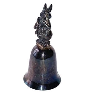 May include: A silver-colored bell with a rabbit figurine on top. The rabbit is holding a bouquet of flowers. The bell has a smooth, reflective surface and a flared base. The rabbit figurine is detailed.