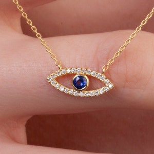 May include: A gold necklace with a blue sapphire eye charm surrounded by small diamonds. The eye charm is in the shape of an almond.