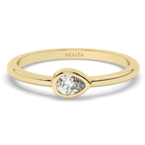 May include: A simple gold band ring with a pear-shaped diamond set in a bezel setting. The ring is inscribed with the word "AZALEA".