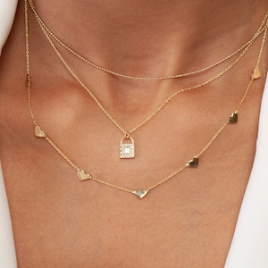 May include: A gold necklace with a padlock pendant and a chain with small heart charms. The padlock pendant is encrusted with clear stones.