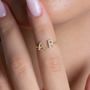 May include: A gold ring with two letters, "A" and "R", set with small clear stones.