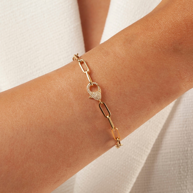 May include: A gold chain bracelet with a pave diamond clasp. The bracelet is made of linked oval shapes.