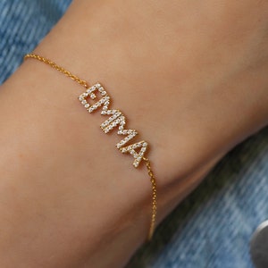 Peut inclure: Un bracelet en chaîne dorée avec le nom "EMMA" écrit en lettres dorées avec de petits diamants sur chaque lettre.