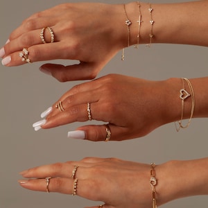 May include: A set of gold jewelry featuring delicate diamond-encrusted rings and bracelets. The jewelry includes a heart-shaped bracelet, a cross bracelet, and several rings with different designs.